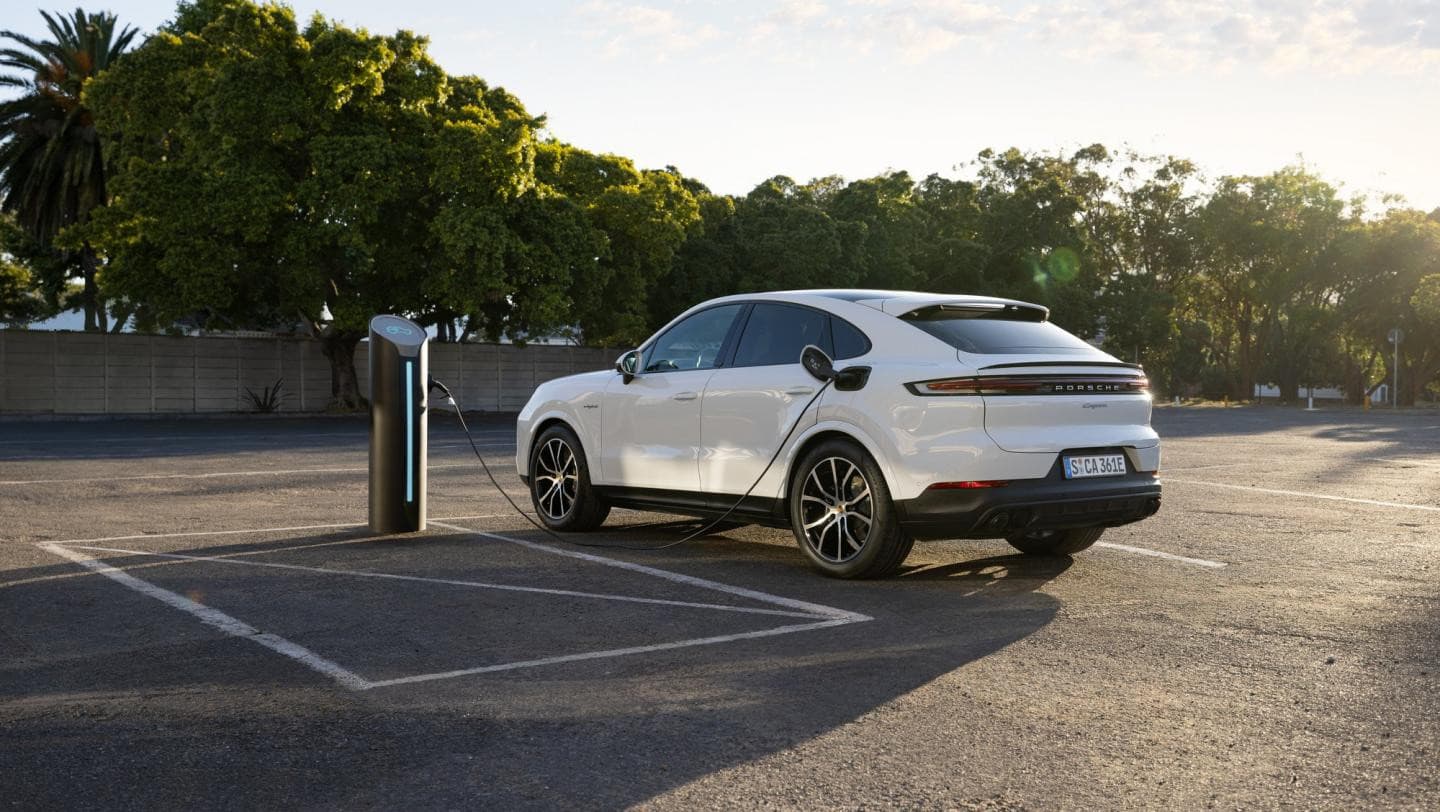 Porsche Cayenne E-Hybrid Coupé blanc branché à une borne de recharge sur un parking ensoleillé