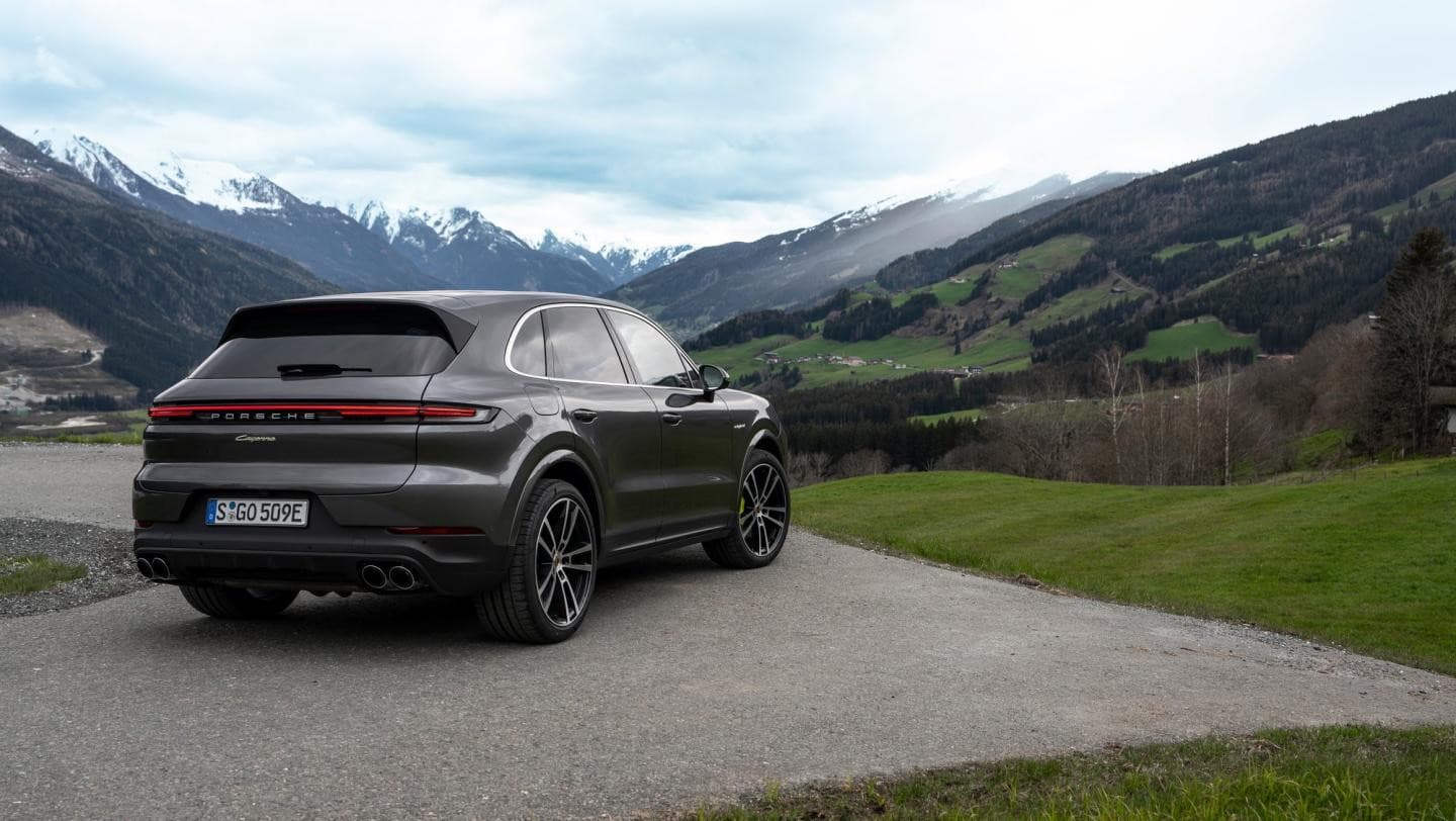 Porsche Cayenne E-Hybrid gris vu de trois quarts arrière devant une vallée de montagne